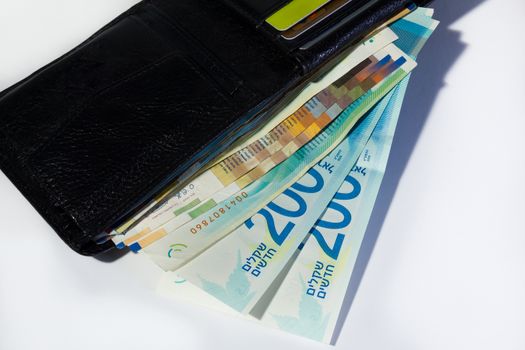 Stack of various of israeli shekel money bills in open black leather wallet - Top view.