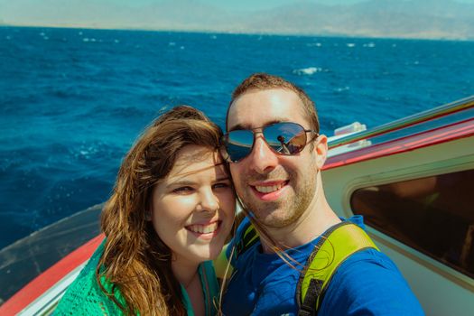 Happy couple sailing on a boat and taking selfie with smartphone or camera.