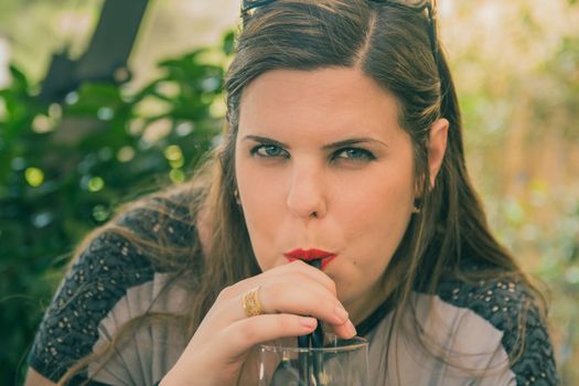 Young woman drink from a glass with drinking straw outdoor.