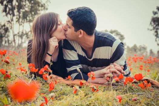 Young couple kissing while lying on the grass in a field of red poppies.