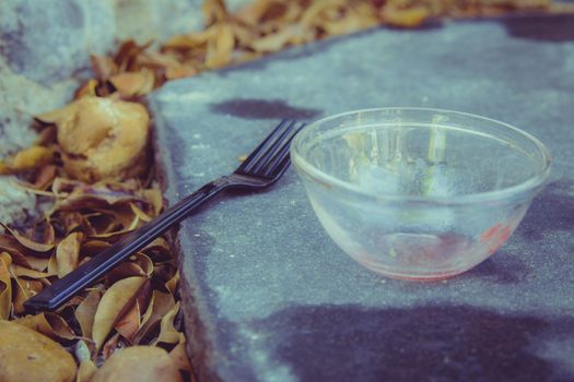 Meal in the garden - Close up on black plastic fork and a small empty glass bowl that are placed on a black stone in the garden. Many orange leaves all around. Selective Focus.

