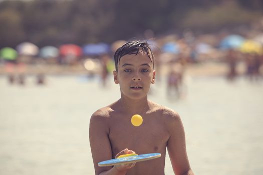 boy with green eyes playing tennis on the beach