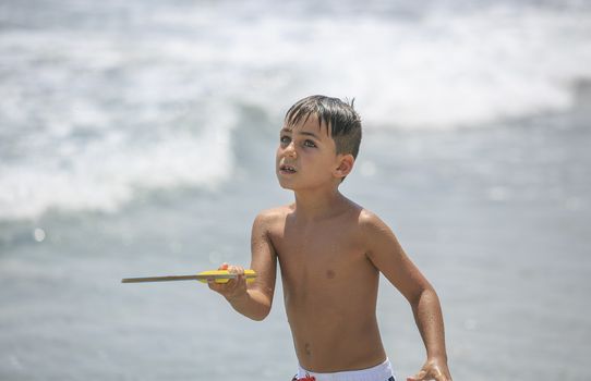 boy with green eyes playing tennis on the beach