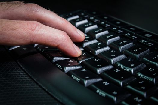 Man typing on a keyboard with letters in Hebrew and English - Wireless keyboard - Dark atmosphere