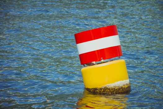 Yellow red and white steel navigational floating buoy in the blue sea water.