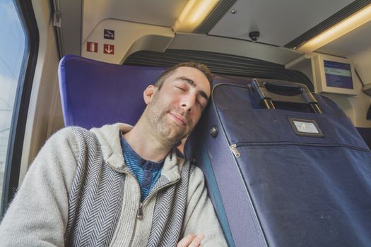 Young man traveling on a train and sleep on blue suitcase next to him.