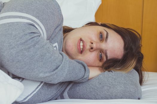 Young woman daydreaming while lying on bed under the blanket.