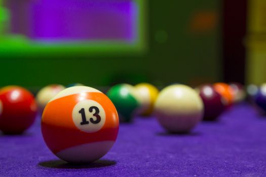 Billiard balls in a pool table. focus on the orange number 13 ball.