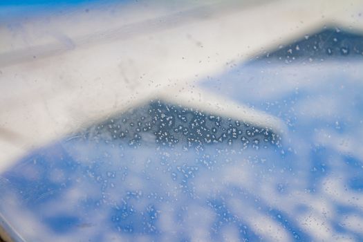 Frozen condensation of ice crystals on the window of an airplane with the wing in the back.