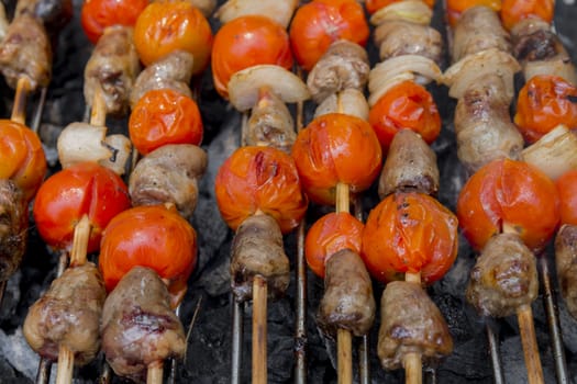 Chicken hearts with tomato and onion cooking on hot grill.