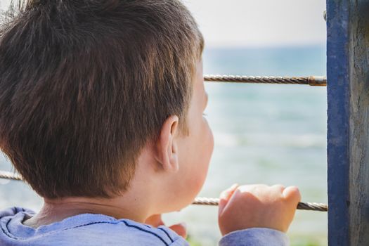 Young boy looks far away to the horizon from behind metal fence.