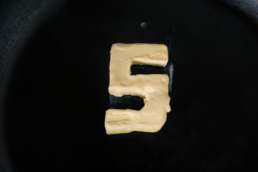 Butter in shape of number 5 on hot pan - Close up top view.
