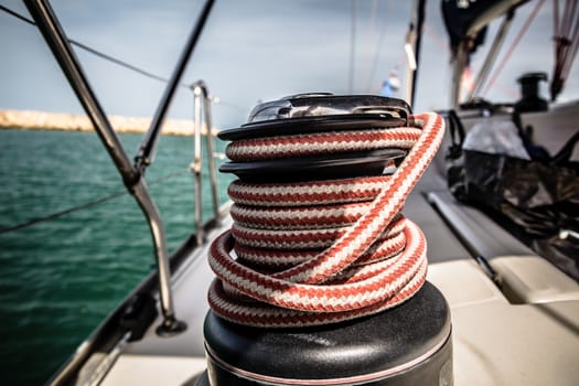 Winch with red and white rope on sailing boat in the sea.