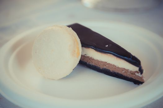 Piece of chocolate-vanilla mousse cake with Glsaz of chocolate and white macaroon on a white plate. 
