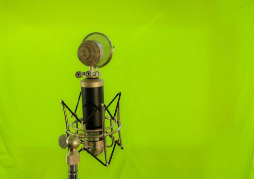 Vocal condenser microphone with wind screen isolated on green background.