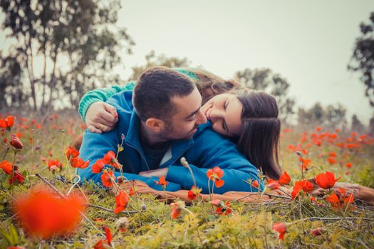 Young couple lying on the grass in a field of red poppies and smiling at each other