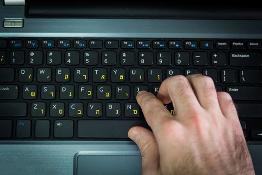 Man typing on a keyboard with letters in Hebrew and English - Laptop keyboard - Top View - Dark atmosphere