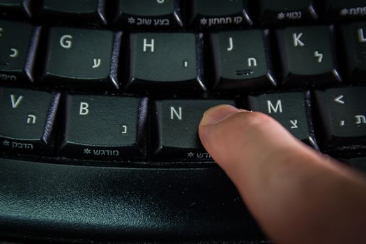 Man typing on a Wireless keyboard with letters in Hebrew and English - Press the New button  - Top View - Dark atmosphere