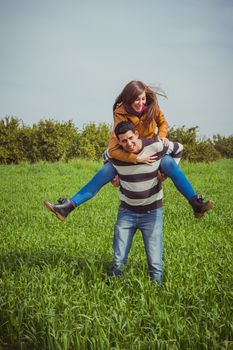 Young couple having fun together in green field. The woman riding piggyback on man shoulders.