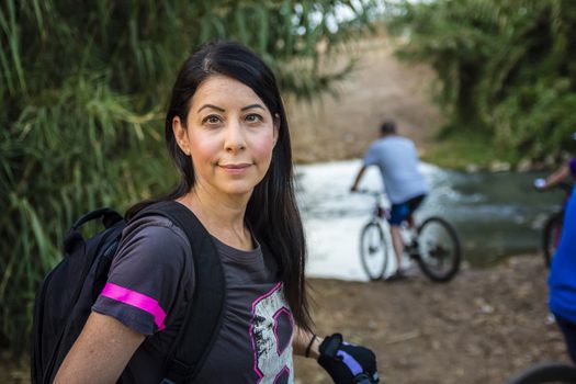 Woman riding a bicycle in the countryside and looking at camera.