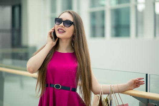 Technologies make shopping easier. Beautiful young woman with shopping bags using her smart phone with smile while standing at the clothing store