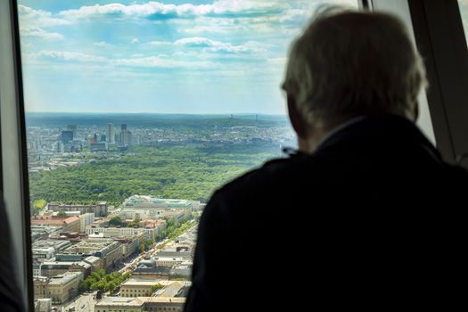 Silhouette of back view of man looking out of a window at the berlin city skyline.