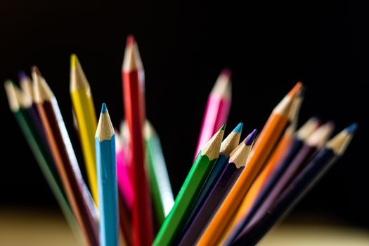 Beautiful and colorful pencil crayons. Wooden table. Black background.