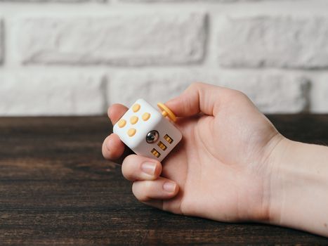 Fidget cube stress reliever in hand over brown wooden background. Fingers antistress toy in hand with copy space.