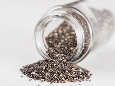 chia seeds scattered from glass jar on white background. Copy space.