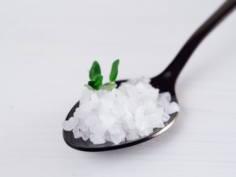 coarse sea salt in black spoon on white background with thyme. Copy space.