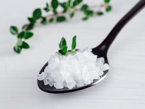 coarse sea salt in black spoon on white background with thyme. Copy space.