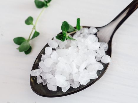 coarse sea salt in black spoon on white background with thyme. Copy space. Top view or flat lay.