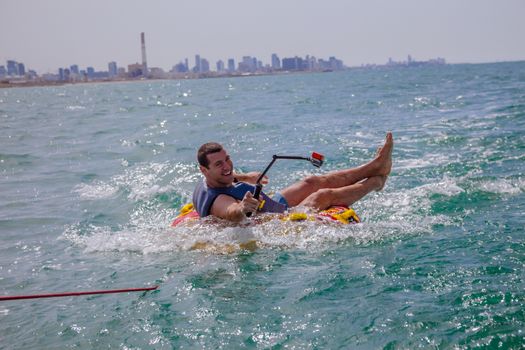 Man sitting in inflatable ring towed by a boat in the water and making faces to the camera and holding Go Pro camera.