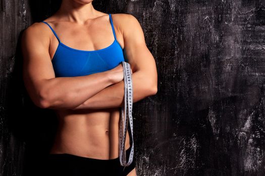 Strong fitness woman with a tape measure on dark background