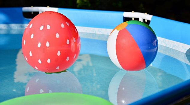 Children playing beach balls floating in swimming pool.