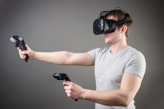 technology, gaming, entertainment and people concept - happy young man with virtual reality headset or 3d glasses with controller gamepad playing racing video game at home