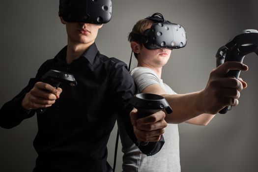 Shot of two young man standing with VR goggles and keep joysticks or finger as a gun