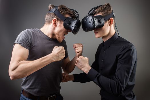 two guys wearing in virtual reality glasses stand face to face and want to fight