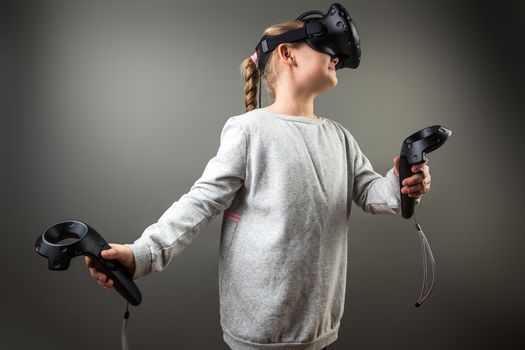 Cute little child girl playing game in virtual reality glasses and two joysticks