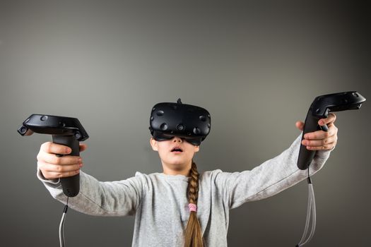 surprised Cute little child girl playing game in virtual reality glasses and two joysticks