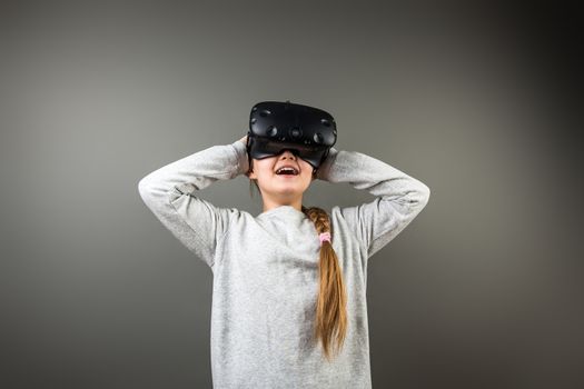 girl wearing virtual reality goggles standing on grey background. VR glasses. 360 degrees. Virtual reality headset. VR game. Wearing virtual reality goggles. Smartphone with VR. Virtual reality video.