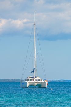 Luxury sailing catamaran in open sea, anchored in shallow water, against plain horizon with clouds