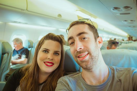 Happy couple taking selfie with smartphone or camera inside airplane.