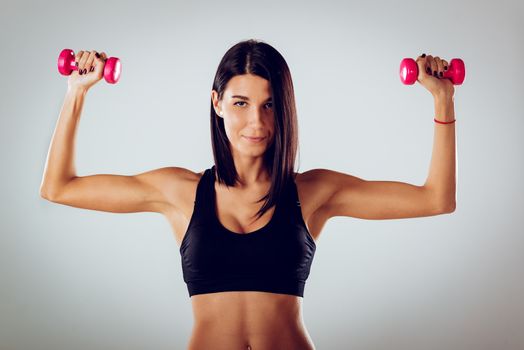 Attractive muscular young woman doing exercise with dumbbells.