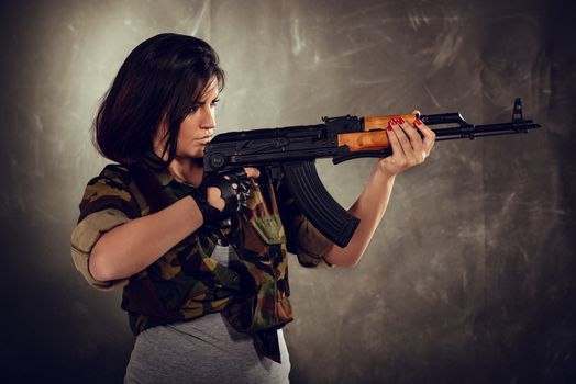 Attractive girl standing in the attitude of aiming and looking through the sight automatic rifle.