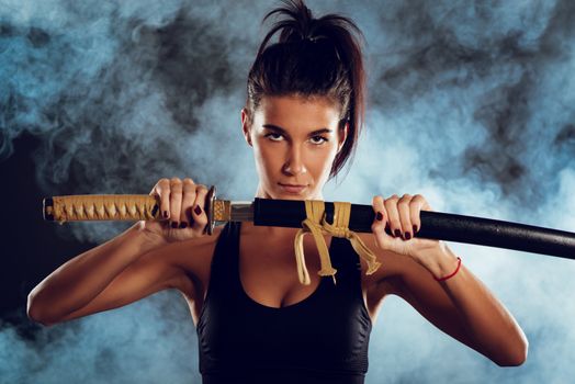 Portrait of a  beautiful young woman holding sword and with a serious expression on her face looking at the camera. 