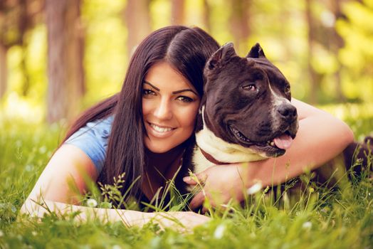 Beautiful young woman hugging her cute stafford terrier in the park and enjoying. Looking at cemera.