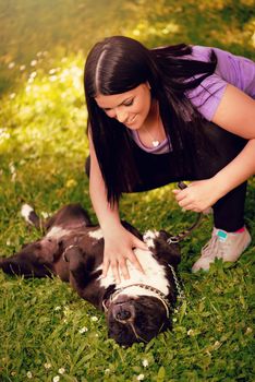 Beautiful young woman playing with her cute stafford terrier in the park.