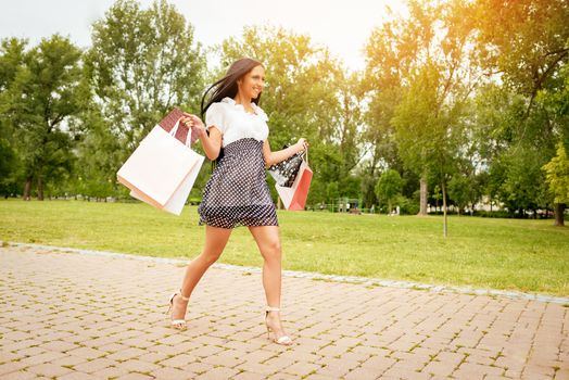 Cheerful young woman running in the park with many shopping bags after successful shopping.
