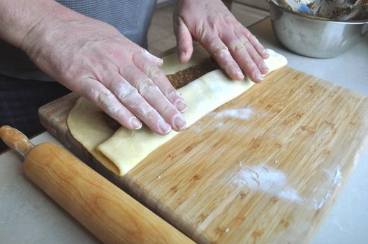 Hands of a Caucasian man rolling a pastry on a wooden board